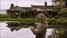 a woman is standing in front of a large house next to a lake .
