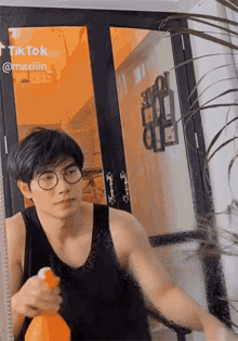 a man wearing glasses and a black tank top is spraying something in front of a door that says tik tok