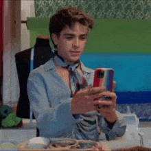a young man is sitting at a table holding a cell phone in his hand .