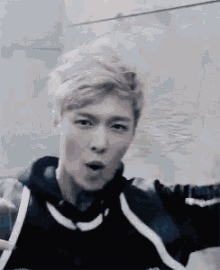a young man with blonde hair is making a funny face while wearing a black jacket .