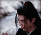 a young man with long black hair is holding a small white rabbit