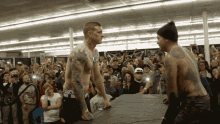 two men are wrestling in front of a crowd and one of them has a tattoo on his back