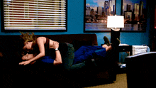 a man and a woman are kissing on a couch in front of a window with blinds