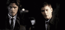 two men in suits and ties are standing next to each other in a dark room holding a badge .