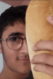 a young man with glasses holds a piece of bread in front of his face