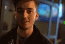 a young man with a beard and a black jacket looks at the camera