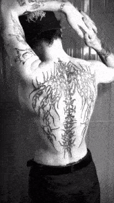 a black and white photo of a man 's back with tattoos
