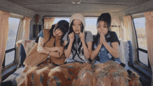 three women are sitting in the back of a van with one wearing a hat