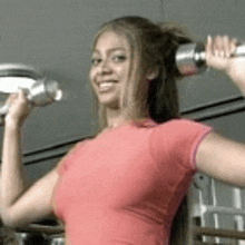 a woman in a red shirt is holding a pair of dumbbells over her head