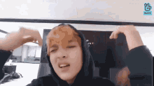 a man wearing a hoodie is making a funny face while sitting in front of a television .