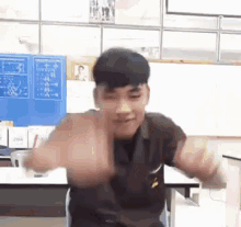 a young man is sitting at a desk with his arms outstretched and making a funny face .