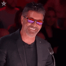 a man wearing sunglasses and a black suit is smiling in front of a microphone