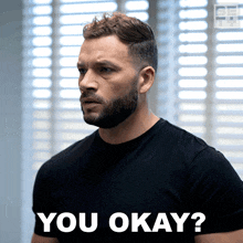 a man with a beard is wearing a black shirt that says " you okay "