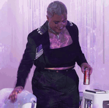 a woman in a black crop top and black pants is holding a can of soda