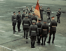 a group of men in military uniforms stand in a line holding a flag