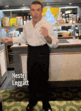 a man in a white shirt and black pants is standing in front of a counter with the name hester leggett written on it