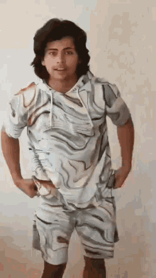 a young man is standing with his hands in his pockets wearing a marbled shirt and shorts .
