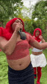 a man in a red wig is singing into a microphone while standing next to another man in a white dress .