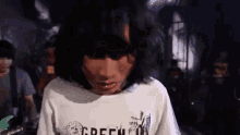 a person with long hair is wearing a white shirt that says green on it .