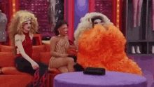 a group of drag queens are sitting on a couch talking to each other .