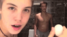 a shirtless man is holding an egg in front of another shirtless man in a bathroom