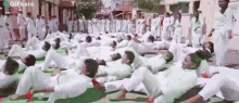 a large group of people in white clothes are doing yoga exercises .