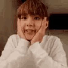 a young boy is sitting at a table with his hands on his face and making a funny face .