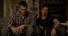 two men are sitting on a couch with bottles of beer in front of them .