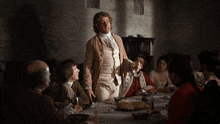 a group of people sitting around a table with a man standing in front of them