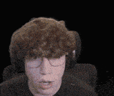 a man wearing glasses and headphones is sitting in a chair with his mouth open .