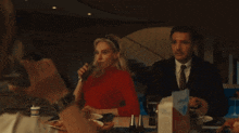 a woman in a red sweater sits at a table with a man and woman