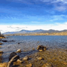 a lake with mountains in the background and rocks on the shore