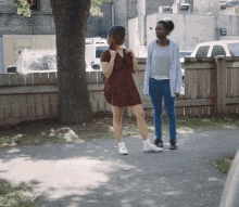 two women are standing on a sidewalk in front of a fence .