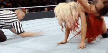 a referee is kneeling down next to a female wrestler who is doing a handstand .