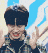 a young man wearing a plaid shirt is smiling and waving
