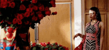 a woman in a zebra print dress is standing in front of a vase of red roses in a room .