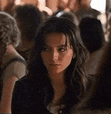 a woman with long dark hair is sitting in a crowd of people .