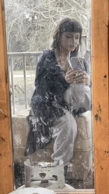 a woman is sitting in front of a window looking at her phone