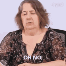 an older woman in a paisley shirt is sitting in a chair and making a funny face .