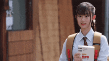 a young girl in a school uniform is holding a book in her hand .