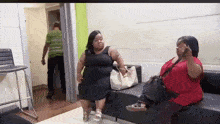 two women are sitting on a couch talking to each other in a room .