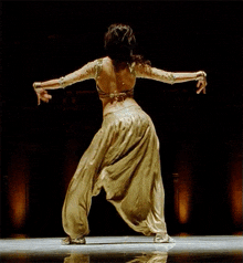 a woman in a gold outfit is dancing with her arms outstretched