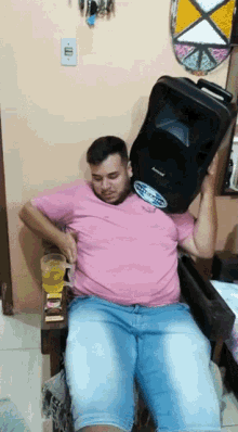 a man in a pink shirt is sitting in a chair holding a speaker over his head that says amphenol on it