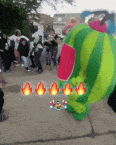 a group of people are gathered on the sidewalk with a green and red balloon with flames around it