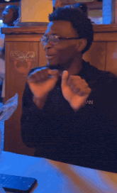 a man wearing glasses sits at a table with a phone and a sign that says juicy crab