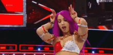 a woman with purple hair is dancing on a stage in a wrestling ring .