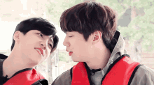 two young men are looking at each other with one wearing a red life jacket
