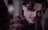 a close up of a young man wearing a plaid shirt and smiling .