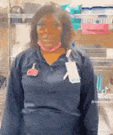 a woman wearing a blue shirt and a pink mask is standing in front of a shelf .