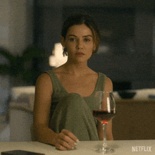 a woman sits at a table with a glass of wine and a netflix logo on the table